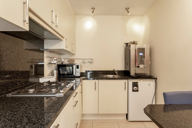 Met een open keukenhoek met een lichte keukeninrichting in een hoekopstelling, voorzien van een granieten aanrechtblad met RVS spoelbak, een RVS gaskookplaat, een afzuigkap, een koelkast en een bijpassende granieten eettafel. 