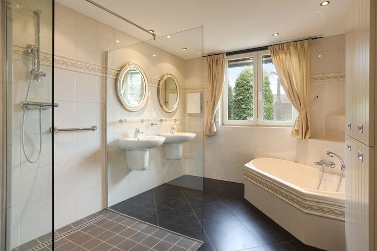 De ruim opgezette badkamer heeft een antraciet tegelvloer met vloerverwarming, volledig licht betegelde wanden en een stucwerk plafond met inbouwspots. Voorzien van een dubbele wastafel met sifonkap en een kunststof ligbad met opzetplateau. 