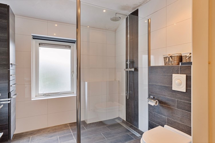 De moderne badkamer is voorzien van een antraciet tegelvloer met vloerverwarming, volledig betegelde wanden en een stucwerk plafond met inbouwspots. Met een wandcloset met opzetplateau en een inloopdouche met regendouche en een thermostaatkraan. 