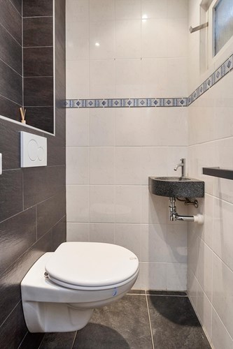 Modern toilet (2013) met een antraciet tegelvloer, volledig betegelde wanden en een kunststof panelen plafond met inbouwspots. Met een wandcloset met opzetplateau en een hoekfonteintje. Natuurlijke ventilatie middels een kunststof raampje. 