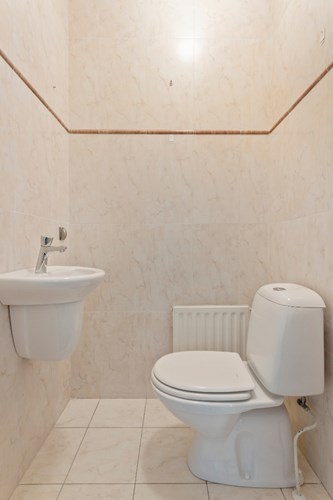 Modern toilet met een lichte tegelvloer, volledig licht betegelde wanden en een stucwerk plafond. Voorzien van een duoblok en een fonteintje. 