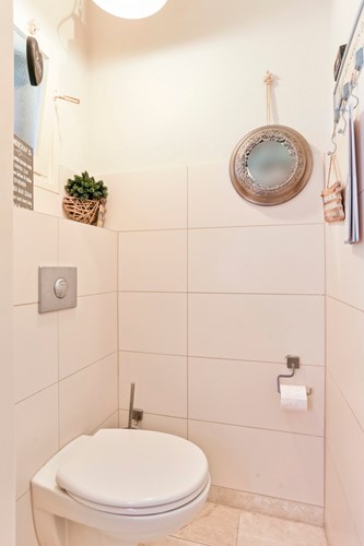 Modern toilet met een marmeren tegelvloer, volledig licht betegelde wanden en een stucwerk plafond met een omlijsting. Voorzien van een wandcloset met een opzetplateau en een raampje. 