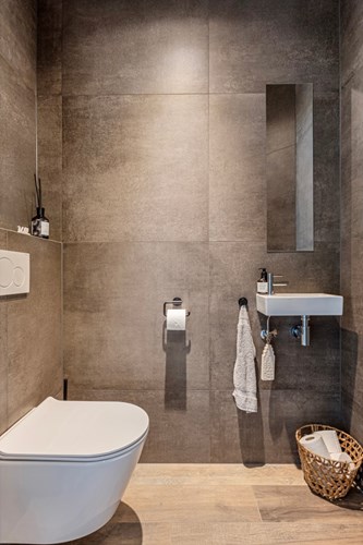 Modern, volledig betegeld toilet met een wandcloset met opzetplateau, een fonteintje en mechanische ventilatie.