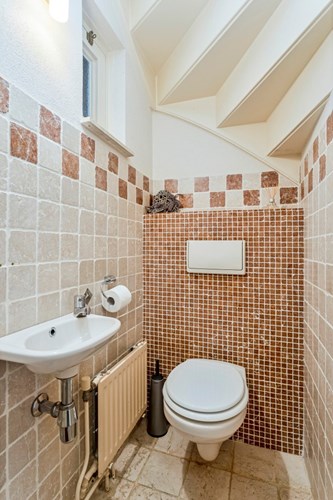 Het toilet is gelegen onder de trapopgang. Met een marmeren tegelvloer en wandtegels. Met een wandcloset met opzetplateau en een fonteintje. Natuurlijke ventilatie middels een hardhouten raampje. 