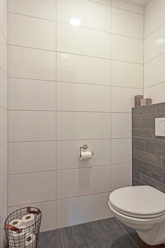 Modern toilet met een antraciet tegelvloer met vloerverwarming, volledig licht betegelde wanden en een stucwerk plafond. Met een wandcloset met opzetplateau en mechanische ventilatie. 