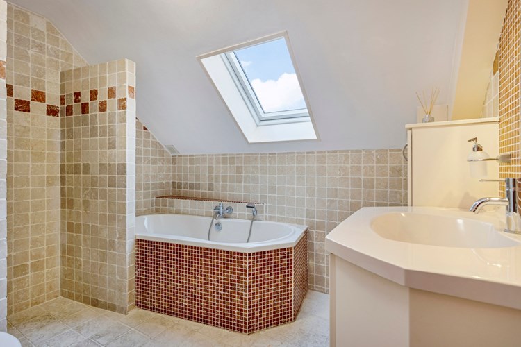 Badkamer met een marmeren tegelvloer met vloerverwarming, marmeren wandtegels en een stucwerk plafond. Voorzien van een duo kunststof ligbad met opzetplateau en een badmeubel met vaste wastafel en een spiegel. 
