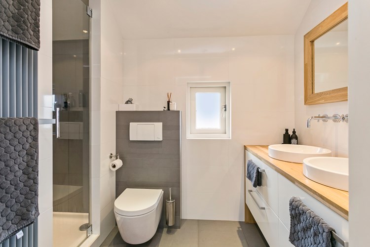 De moderne badkamer is volledig licht betegeld met een stucwerk plafond met inbouwspots. Met  een wandcloset met opzetplateau.