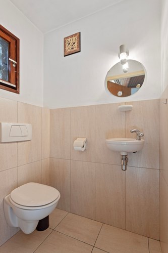 Toilet met een lichte tegelvloer met vloerverwarming, gedeeltelijk betegelde wanden en een stucwerk plafond. Met een wandcloset met een fonteintje en een raampje. 