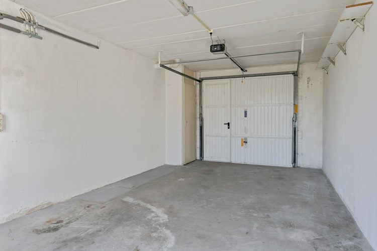 Garage met een betonvloer, stucwerk wanden en een betonnen dak. Via een op afstand te bedienen stalen kantelpoort met loopdeur naar de bestrate oprit. Hier bevindt zich ook de meterkast (o.a. 7 groepen + 2x aardlekschakelaar) en de Remeha Avanta HR combiketel (2015). 