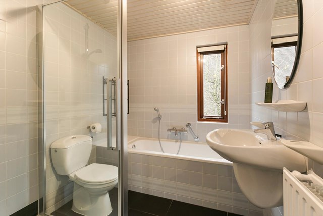 De badkamer is geheel betegeld en beschikt over een natuurlijke ventilatiemogelijkheid door het boven het ligbad geplaatste raamkozijn.