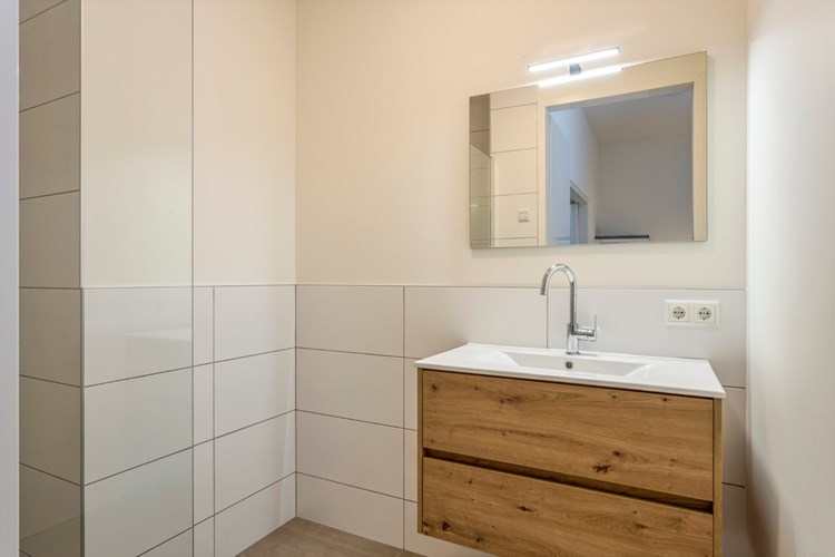 Via een deur in de keuken naar de moderne badkamer met een tegelvloer met vloerverwarming en stucwerk wanden. Met een badmeubel met een wastafel en spiegel.