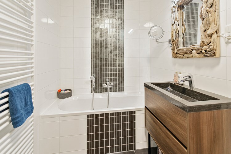 De volledig betegelde, moderne badkamer is o.a. voorzien van een ligbad en een designradiator.