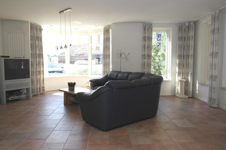 De riante woonkamer is voorzien van een lichte tegelvloer met vloerverwarming, stucwerk wanden en een stucwerk plafond. 