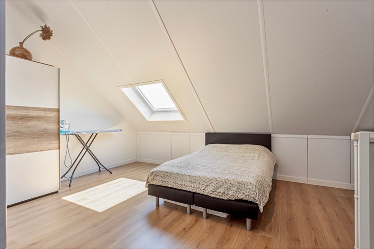 Een royale zolder (slaap-)kamer met een laminaatvloer en bergruimte in de schuinten. 
