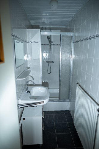 Badkamer met een antraciet tegelvloer en volledig licht betegelde wanden. Voorzien van een douchecabine met thermostaatkraan en een wastafel met spiegel. 