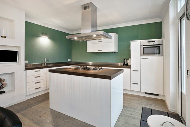 De moderne keuken heeft een kookeiland en keukenblok in hoekopstelling, met apothekerskast en voorzien van modern  inbouwapparatuur.
