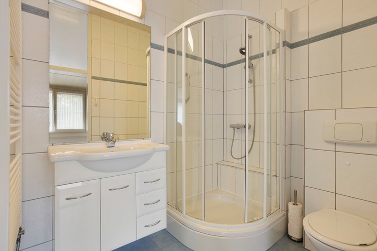 Een volledig betegelde badkamer met een MDF plafond. Voorzien van een badmeubel met een vaste wastafel en een grote spiegel, een douchecabine met thermostaatkraan en een wandcloset met een opzetplateau. Mechanische ventilatie is aanwezig. 