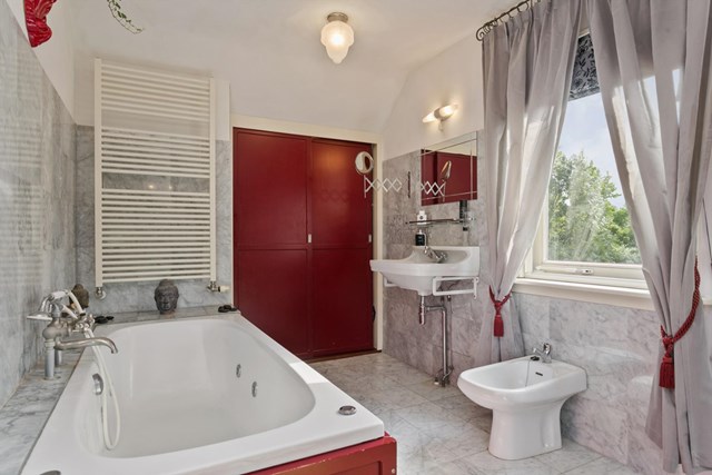 De badkamer met ligbad, wastafel, bidet en chique marmeren betegeling. 