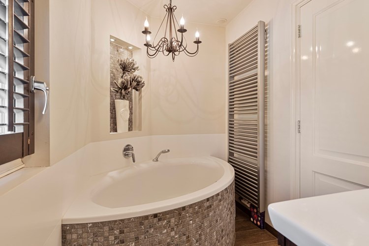 Moderne, sfeervolle badkamer met een tegelvloer, gedeeltelijk betegelde en gestucte  wanden en een stucwerk plafond. Voorzien van een kunststof 2-persoons hoekbad met een geïntegreerde thermostaatkraan en een designradiator. 