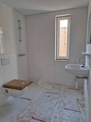 Een volledig betegelde badkamer met vloerverwarming voorzien van een inloopdouche, een wandcloset en een wastafel. Hier bevinden zich ook de aansluitingen voor de wasapparatuur. 