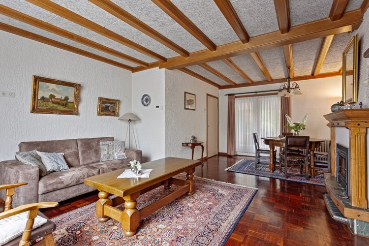De woonkamer is voorzien van een parketvloer, behangen- en stucwerk wanden en een sierbalken plafond. 