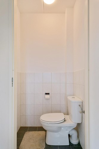 Separaat toilet met een tegelvloer, gedeeltelijk betegelde wanden en een spuitwerk plafond. Voorzien van een duoblok en mechanische ventilatie. 