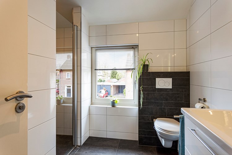 Luxe badkamer (2017) met een antraciet tegelvloer, volledig licht betegelde wanden en een stucwerk plafond. Met een wandcloset met opzetplateau en een inloopdouche met een glazen deur, een thermostaatkraan en een regendouche. 