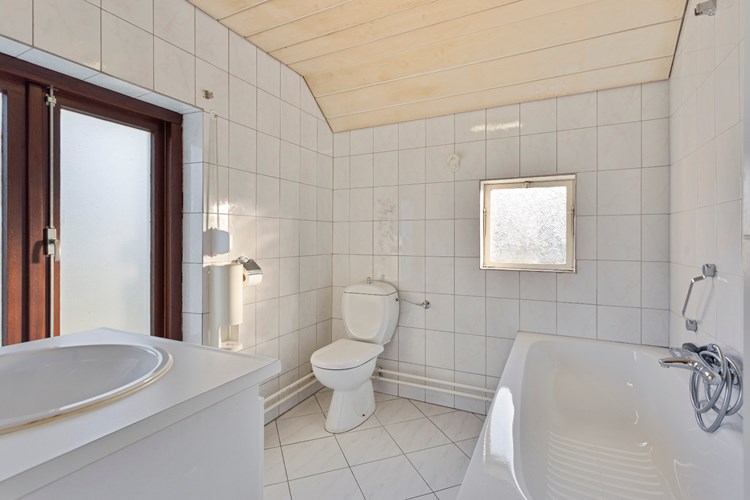 Badkamer met een lichte tegelvloer, volledig licht betegelde wanden en een MDF plafond. Met een ligbad en een 2e toilet. 
