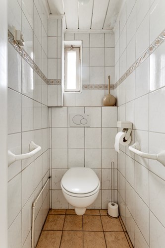 Toilet met een tegelvloer, volledig licht betegelde wanden en een MDF plafond. Met een wandcloset met een opzetplateau en een raampje.