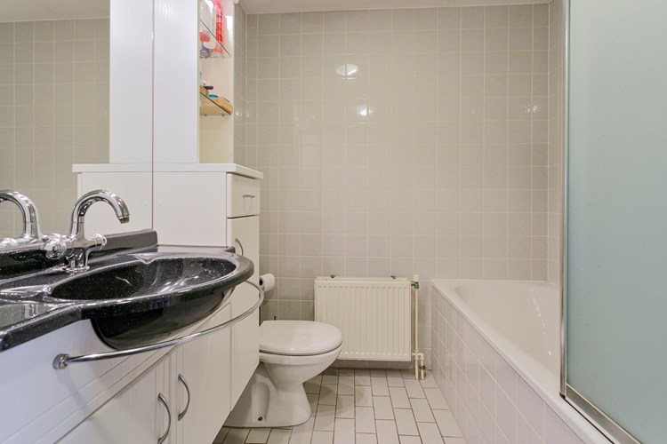 Badkamer met een lichte tegelvloer, volledig licht betegelde wanden en een spuitwerk plafond. Met een 2e toilet, een badmeubel met vaste wastafel en een spiegel met inbouwspots. 
