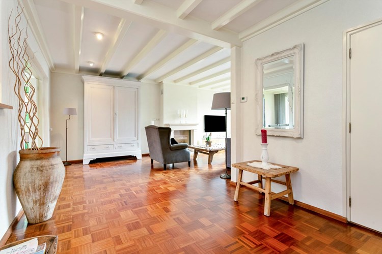 De woonkamer is voorzien van een parketvloer, spachtelputz wanden en een licht sierbalkenplafond. 