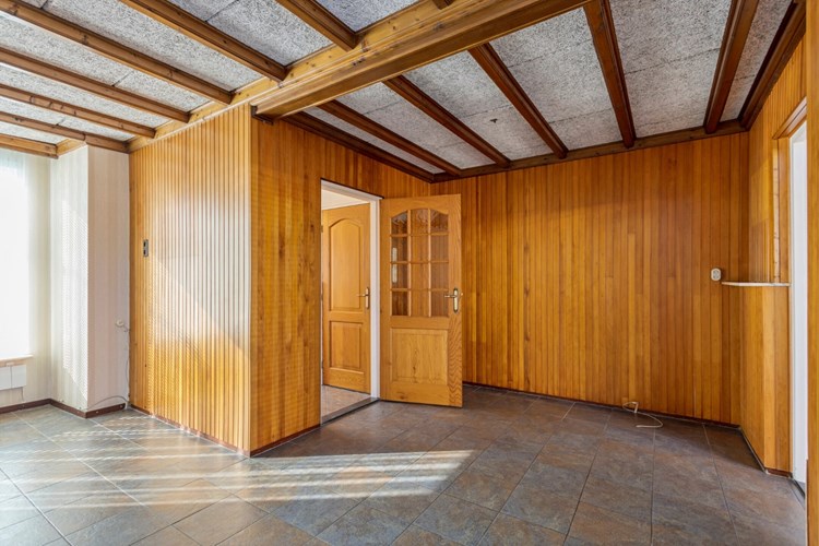 Vanuit de entree met een deur naar de woonkamer met een tegelvloer,  behang- en schroten wanden en een sierbalkenplafond met HWC platen. 