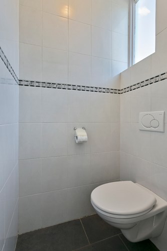 Modern toilet met een antraciet tegelvloer met vloerverwarming, volledig licht betegelde wanden en een stucwerk plafond. Met een wandcloset en een hardhouten raampje. met dubbele beglazing. 