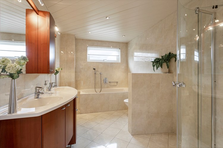 De ruime badkamer is volledig licht betegeld, met een aluminium plafond met inbouwspots. Voorzien van een badmeubel met dubbele wastafel en een kunststof ligbad met geïntegreerde Grohe thermostaatkraan. 