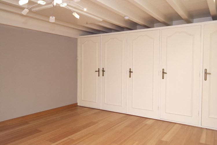 Ruime slaapkamer met een laminaatvloer, structuurverf wanden en een licht balken plafond en met een vaste kastenwand. 