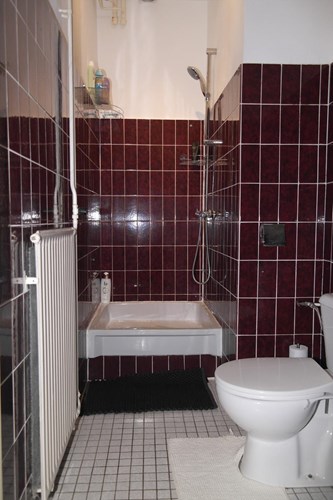 Badkamer met een tegelvloer en grotendeels betegelde wanden. Voorzien van een toilet en een douche met thermostaatkraan.
