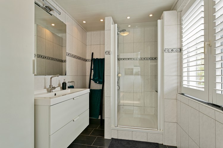 Via de keuken rechtstreeks toegang tot de volledig betegelde badkamer met een panelen plafond met inbouwspots. Met een douchecabine met douchedeur, een plateautje en een thermostaatkraan, een badmeubel met wastafel en spiegel. Kunststof raamkozijn met dubbele beglazing en shutters.