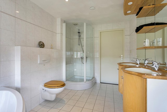 De badkamer is geheel betegeld en heeft naast het hoekbad ook een separate douche, dubbele wastafel en vrijhangend toilet.