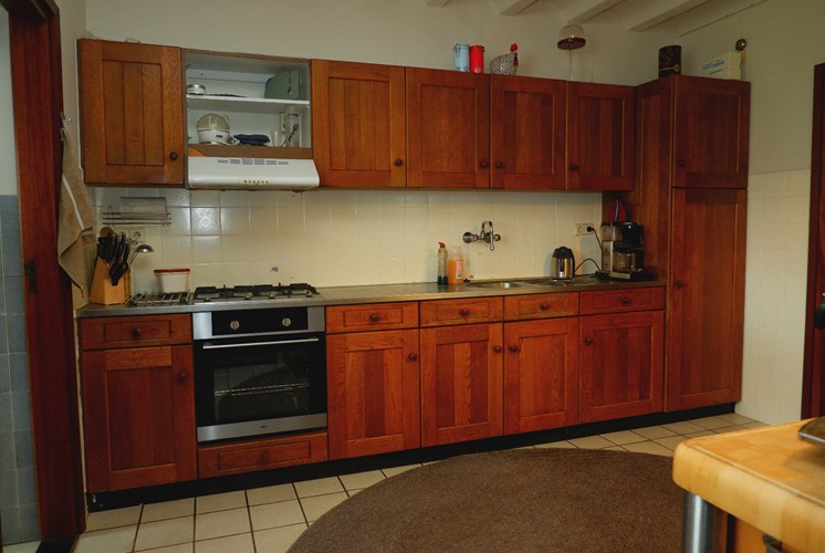 Een ruime keuken met een tegelvloer is voorzien van een eiken keukeninrichting met een 4 pits gaskookplaat, een afzuigkap en een grote koelkast.