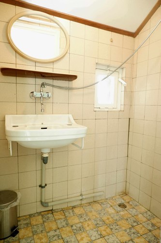 Doucheruimte met een tegelvloer, volledig licht betegelde wanden. Met een douche en een wastafel. Natuurlijke ventilatie middels een raampje. 