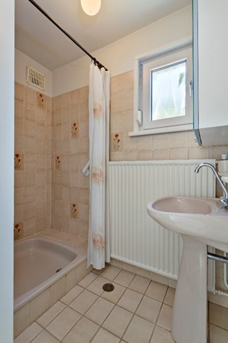 Een doucheruimte met grotendeels betegelde wanden en een stucwerk plafond. Met een douche met thermostaatkraan en een wastafel op zuil. Daglicht en natuurlijke ventilatie middels een kunststof raampje met dubbele beglazing en een rolluik. 