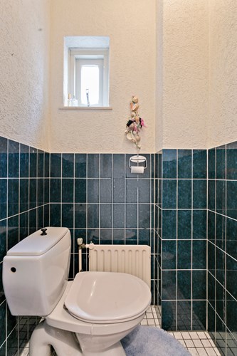 Toilet met een lichte tegelvloer, gedeeltelijk betegelde wanden en een stucwerk plafond. Voorzien van een duoblok en een raampje. 