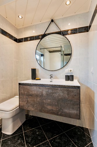Badkamer met een tegelvloer met vloerverwarming (indirect via radiator), volledig licht betegelde wanden en een MDF plafond met inbouwspots. Voorzien van een badmeubel met vaste wastafel en een toilet (sanibroyeur).