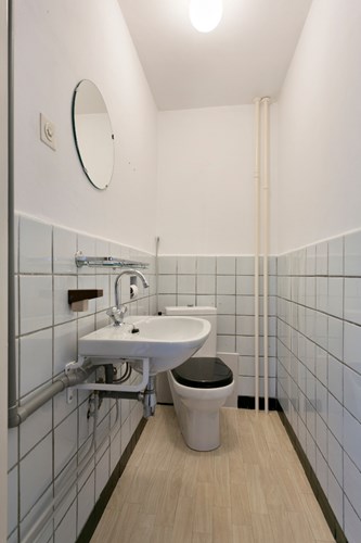 Het separaat toilet is gedeeltelijk betegeld en voorzien van een duoblok en een wastafel.