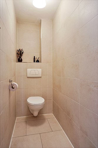 Separaat toilet met een lichte tegelvloer, volledig licht betegelde wanden en een stucwerk plafond. Voorzien van een wandcloset met opzetplateau. 