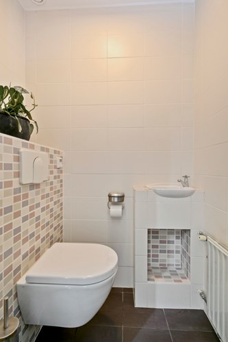 Modern toilet met een tegelvloer, volledig licht betegelde wanden en een stucwerk plafond. Met een wandcloset met een opzetplateau, een fonteintje en mechanische afzuiging. 