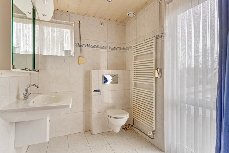 De badkamer is voorzien van een lichte tegelvloer, volledig licht betegelde wanden en een MDF plafond met inbouwspots. Met een wandcloset met opzetplateau en een vaste wastafel met een spiegelkast. 