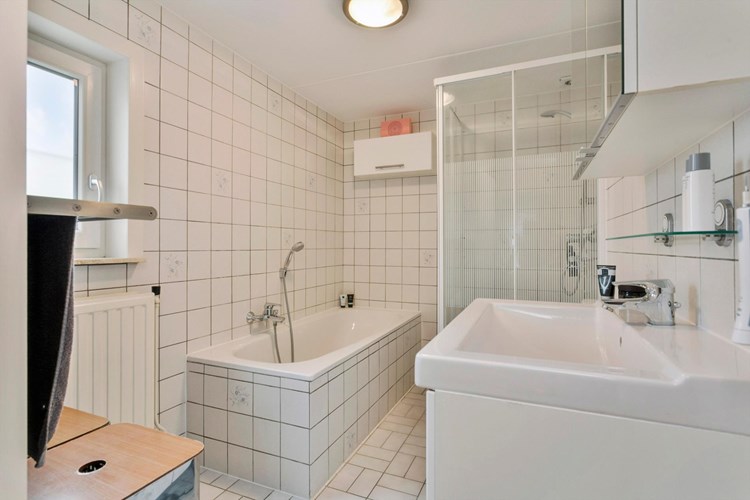 Volledig, licht betegelde badkamer en een spuitwerk plafond. Met  een ligbad en een badmeubel met vaste wastafel en een spiegelkast. 