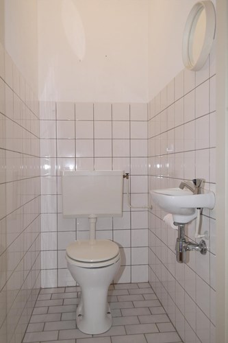 Toilet met een lichte tegelvloer, gedeeltelijk betegelde wanden en een spuitwerk plafond. Met een duoblok, een fonteintje en mechanische ventilatie. 