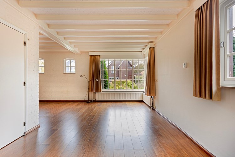 Met een parketvloer, licht getexte schoonmetselwerk wanden, waarvan één wand is behangen en een licht sierbalken plafond. 